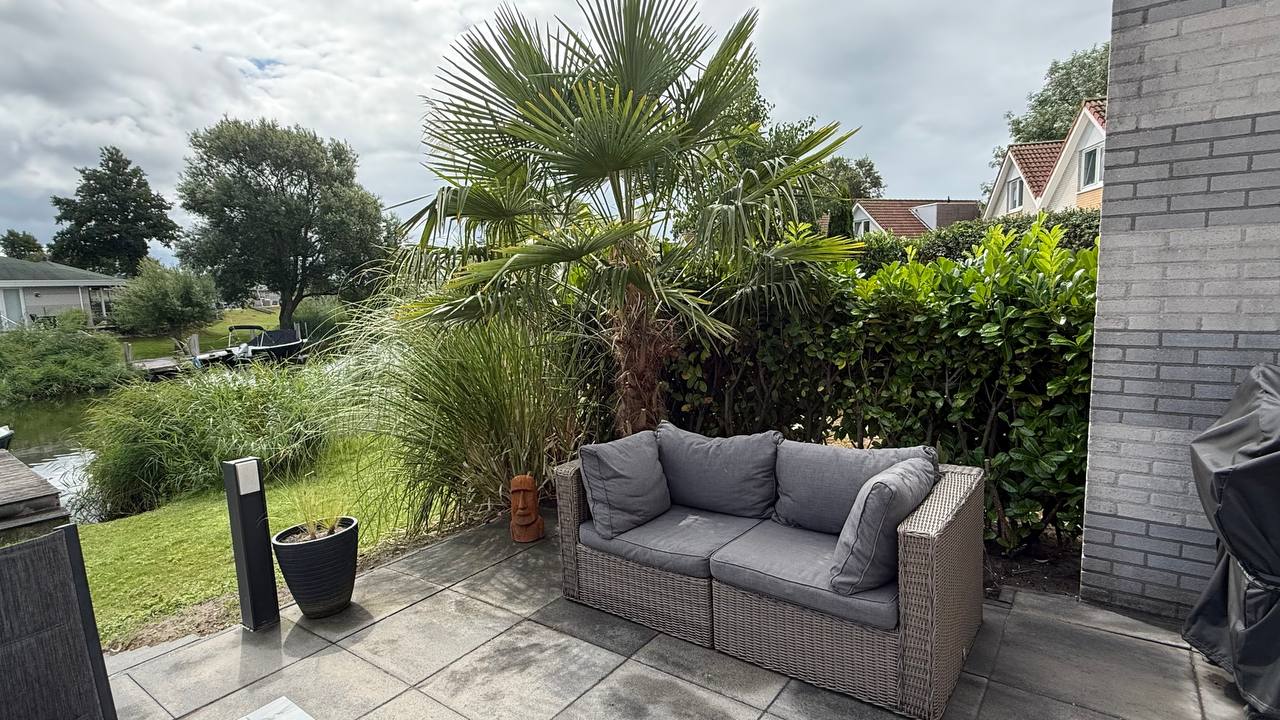 Lounge-Couch mit grünem Kissen unter Palmenblättern in der Schakelvilla